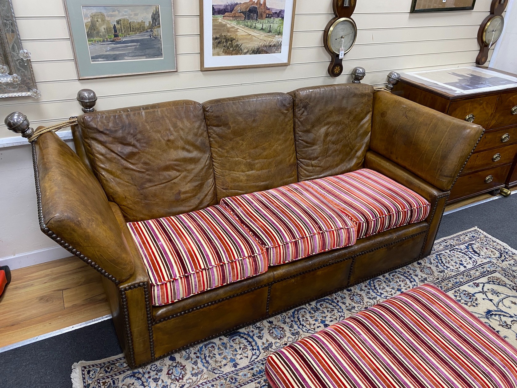 A studded tan leather Knowle settee with striped fabric loose cushion seat, length 220cm, depth 96cm, height 110cm and matching footstool, width 104cm, depth 64cm